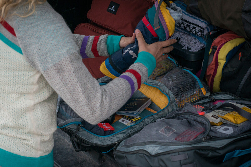 A woman packing a Cotopaxi Batac backpack into a vehicle