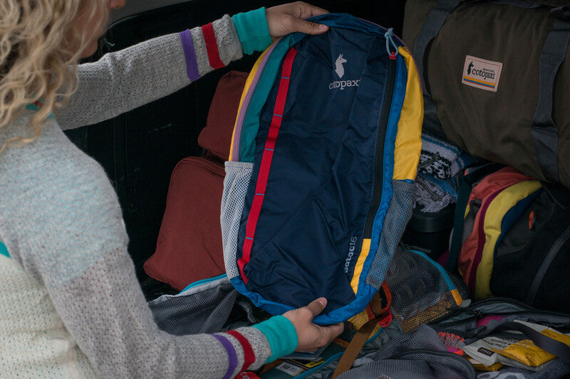Woman accessing the contents of a Cotopaxi Batac backpack by a car